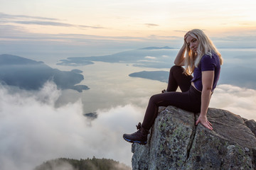 Adventurous Female Hiker on top of a mountain covered in clouds during a vibrant summer sunset. Taken on top of St Mark's Summit, West Vancouver, British Columbia, Canada.