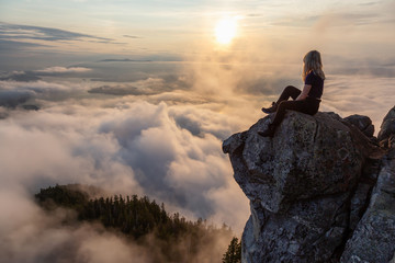 Adventurous Female Hiker on top of a mountain covered in clouds during a vibrant summer sunset. Taken on top of St Mark's Summit, West Vancouver, British Columbia, Canada.