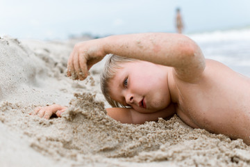 A little boy is digging in the sand on the beach.
