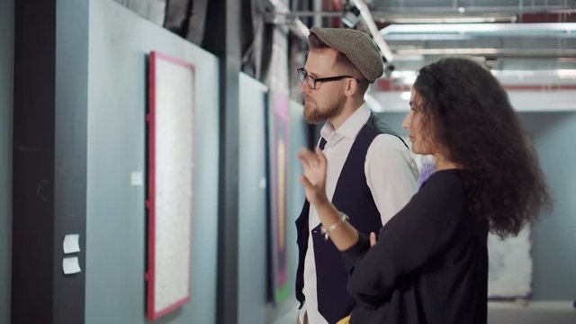 Two young visitors of art exhibition are discussing a picture in a hall