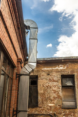 Metal air duct from the kitchen of the restaurant , laid on a brick wall . The courtyard of the old house . Site about  architecture , kitchen .