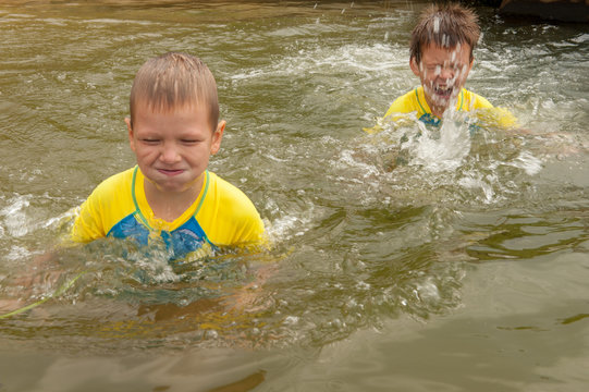 Funny children in swimsuits accelerate on wooden bridge near river and jump into water. boys are happy on holiday in village together. Summer day, river, swimming in water