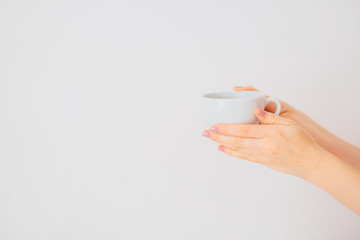 Female hands with neat manicure holding a cup of coffee on a white background. Copy space.