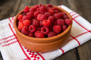 Fresh organic raspberries in a clay bowl on old wooden table