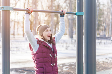 Attractive girl involved in sports workout on a horizontal bar on a sunny winter day. The concept of sports activities all year round