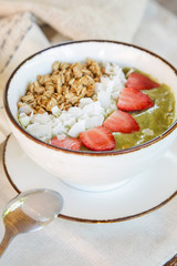 Delicious organic green smoothie bowl garnished with strawberries, sliced almonds and granola