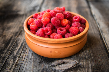 Fresh organic raspberries in a clay bowl on old wooden table