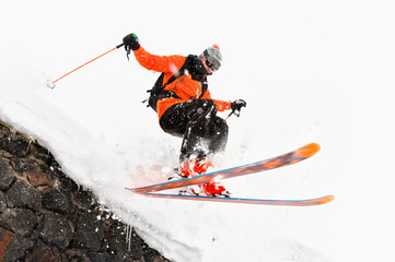 The athlete skier on a light background with a jump moves off the roof of a snow-covered hut with flying flakes of snow. The concept of winter ski sports