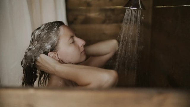 Beautiful young woman relaxing under shower in outdoor bathroom