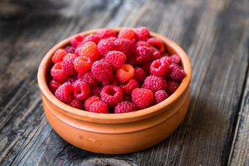 Fresh organic raspberries in a clay bowl on old wooden table