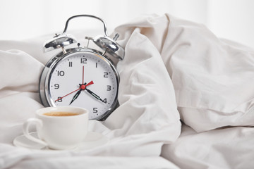 coffee in white cup on saucer near silver alarm clock in white blanket