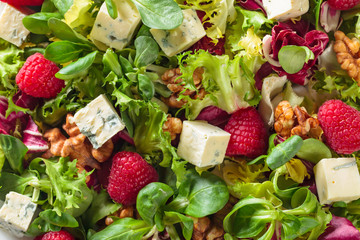 Green salad with slices of blue cheese , raspberries and nuts.