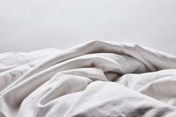 crumpled white blanket in bed isolated on grey