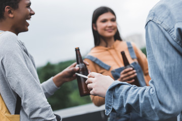 selective focus of teenagers holding glass bottles with beer and smoking cigarette