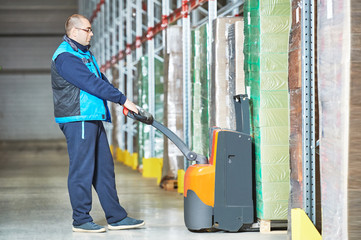 Worker with pallet truck stacking cardboxes © Kadmy