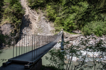 View of a wild river in a gorge with a modern hanging bridge in the Swiss Alps