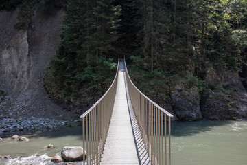 Fototapeta premium View of a wild river in a gorge with a modern hanging bridge in the Swiss Alps