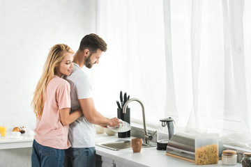 Fototapeta na wymiar beautiful woman hugging man washing dishes at kitchen