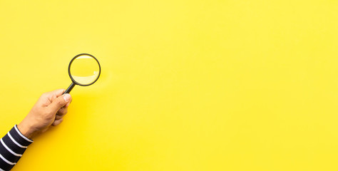 Searching concepts with male hand using magnifying glass on yellow space background - obrazy, fototapety, plakaty