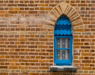 Detailed close up of an old, weathered, blue painted wooden lancet window in textured newly pointed brick wall. Coloured wooden shingles. Space for copy. Landscape image. England. 