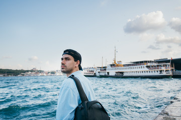 Fototapeta premium Portrait of a young man against the background of the sea, city, pier and ships.
