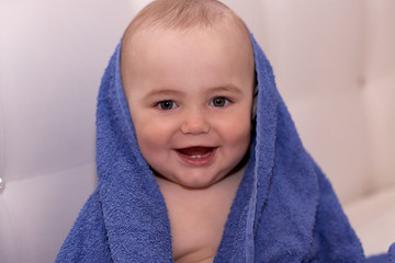 Baby after bath sits wrapped in a towel