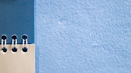 Background. Part of an open notebook on a blue painted plastered wall
