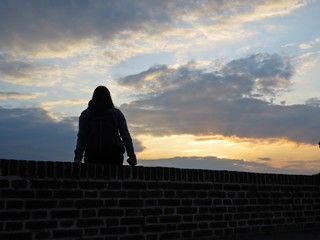 One Single Woman Silhouette Sitting on Brick Wall during Sunset with Cloudy Sky in Background