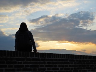 One Single Woman Silhouette Sitting on Brick Wall during Sunset with Cloudy Sky in Background