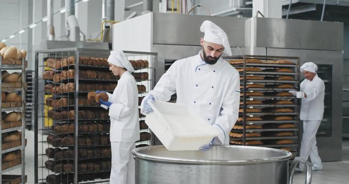 Big bakery industry baker prepare the dough add the flour in a big container background workers arrange the bread and transported the baked bread