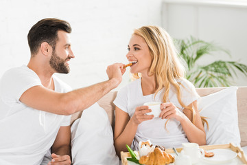 Obraz na płótnie Canvas beautiful couple in pajamas having breakfast in bed in morning