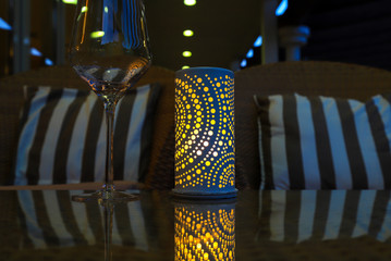 Lamp on the holiday table in the evening dinner. Elegant blue lantern with a yellow candle on a glass table and a transparent glass at night.