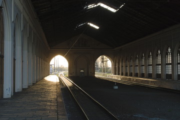 Naklejka na ściany i meble Railway tracks under the roof of the station. The light of the sun penetrates through the arches in the wall. Waiting for the train to arrive before the trip.