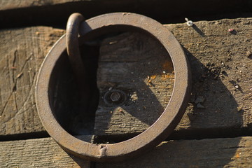 Old rusty metal ring for mooring ships in wooden pier flooring. Close up.