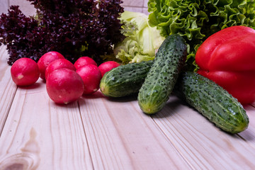 fresh vegetables on a light wooden table, paprika, celery, leaves of lettuce, cucumbers and radishes