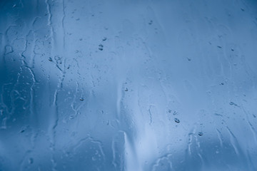 Drops of rain on the glass against the blue cloudy sky. Time before a thunderstorm. Close-up with selective focus. Abstract background