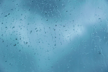 Drops of rain on the glass against the blue cloudy sky. Time before a thunderstorm. Close-up with...