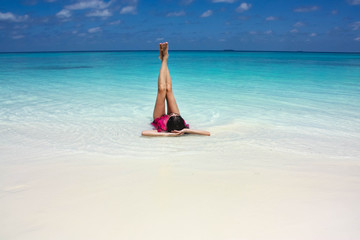 a young woman lies on the white sand near the turquoise water and rests/relaxing. Paradise beach maldives
