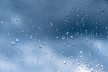Drops of rain on the glass against the blue cloudy sky. Time before a thunderstorm. Close-up with...