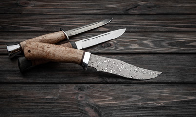 Hunting bowie knife with a wooden handle on dark wooden background. Steel arms weapon. top view