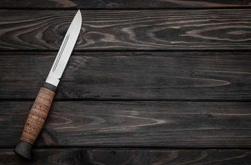 Hunting bowie knife with a wooden handle on dark wooden background. Steel arms weapon. top view