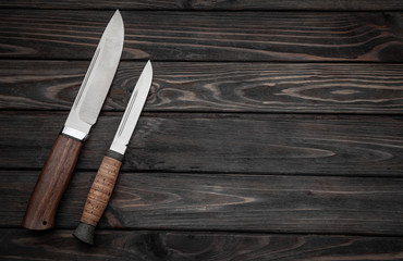 Hunting bowie knife with a wooden handle on dark wooden background. Steel arms weapon. top view