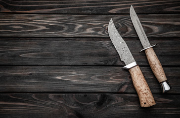 Hunting bowie knife with a wooden handle on dark wooden background. Steel arms weapon. top view