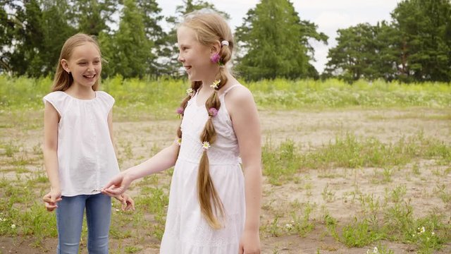 Two girl friends having fun on green lawn while summer vacation. Tenager girls laughing on green meadow while summer walk. Summer activity