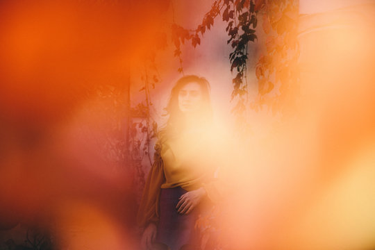 Blurry photo of young woman on autumn street with colorful leaves around. Orange leaves have fallen and are scattered around. Sunny day.