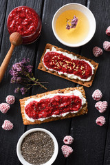 Healthy sugar free dessert and herbal tea. Raspberry chia jam on crispy bread and cream cheese with frozen berries on black background