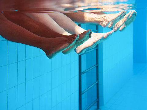 four people legs underwater in the swimming pool. Party. Summer. Vacation, diversity, friendship and sport concept.