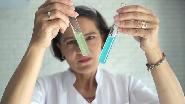 Woman scientist looking at chemicals in test tube at lab, slow motion