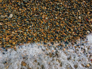 Sea wave foam on coastal pebbles.