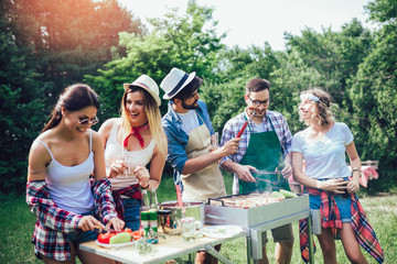 Young friends having fun grilling meat enjoying barbecue party.